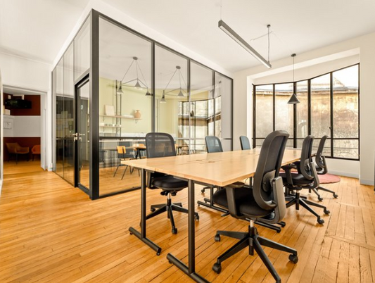 Table de réunion et fauteuils reconditionnés dans un bureau vitré au parquet clair, séparé du plateau par des cloisons verrière