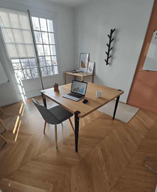 Bureau individuel en bois dans une pièce parisienne au parquet à chevrons, avec portemanteau mural et tableau blanc